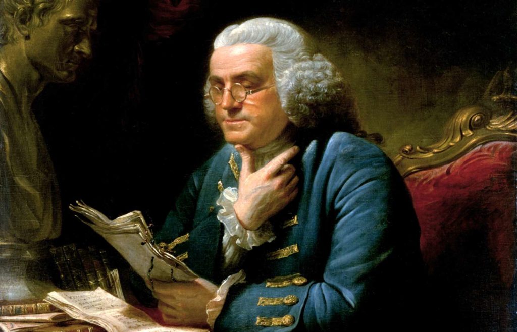 Painting of Benjamin Franklin in a blue coat, reading papers at his desk with his chin on his hand